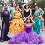 A group of women in Disney character costumes posing outdoors, embodying iconic princesses.