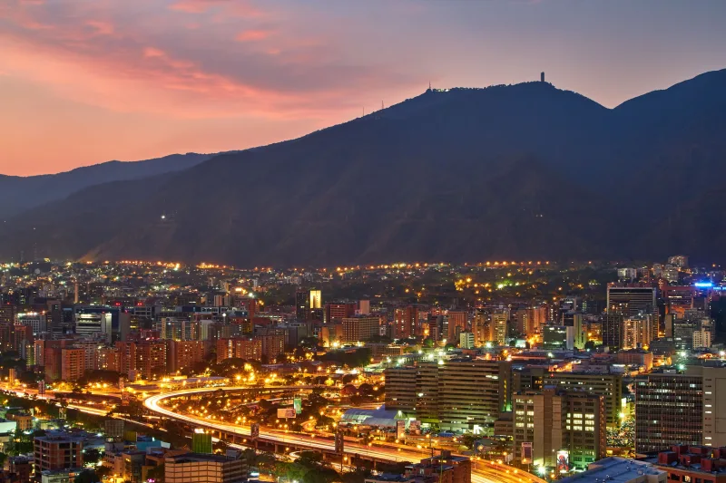 A stunning aerial view of Caracas cityscape at dusk, showcasing the vibrant city lights against the mountainous backdrop.