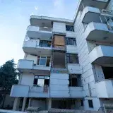 Low angle shot of a damaged residential building exterior with visible balconies and wear.