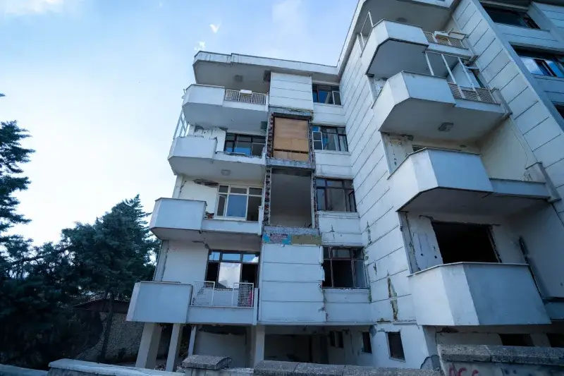 Low angle shot of a damaged residential building exterior with visible balconies and wear.