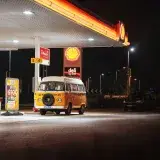 A classic orange van parked at a Shell gas station under bright lights at night.