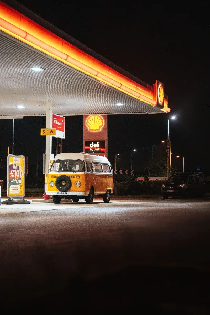 A classic orange van parked at a Shell gas station under bright lights at night.