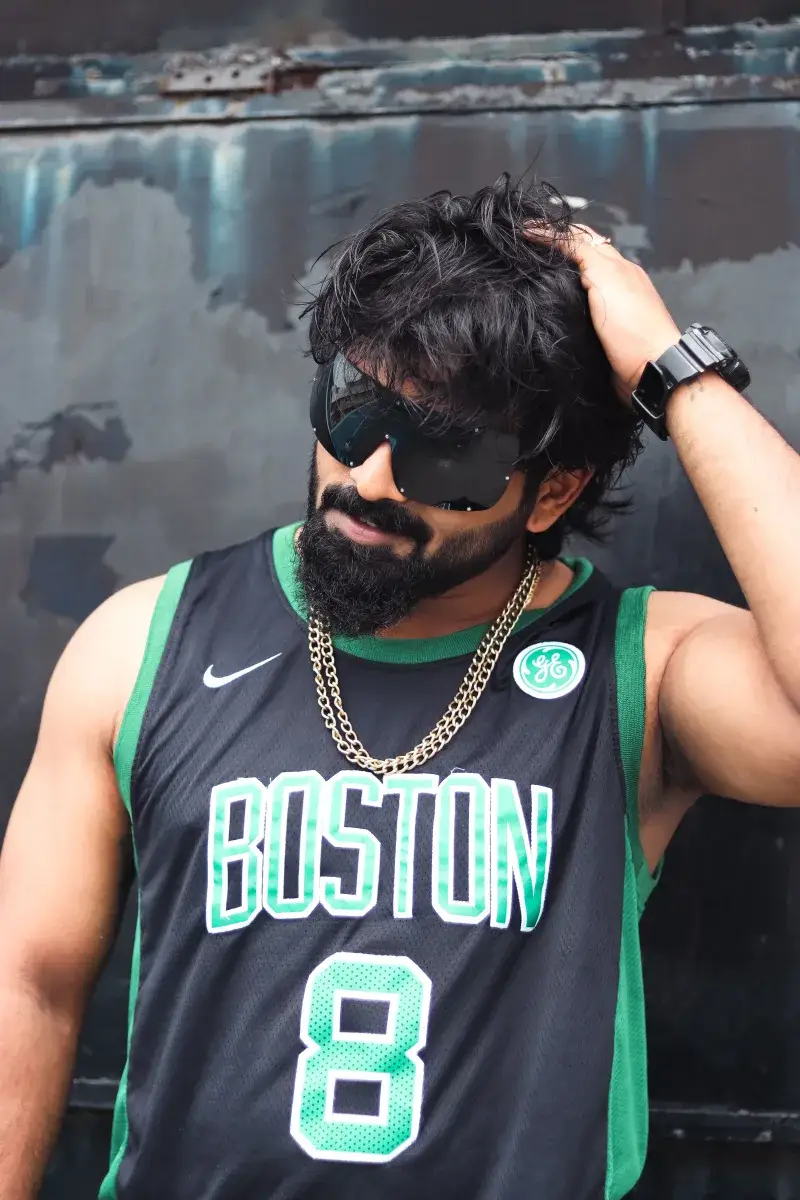 Retrato de un hombre a la moda con ropa deportiva de Boston Celtics, gafas de sol y collar, exudando estilo fresco.
