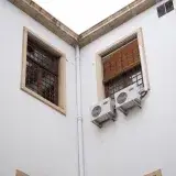 White building facade with wooden window shades and air conditioning units.