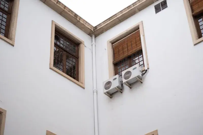 White building facade with wooden window shades and air conditioning units.