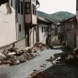 Devastation from an earthquake shown on a narrow village street in Malatya, Turkey, with debris and ruined buildings.