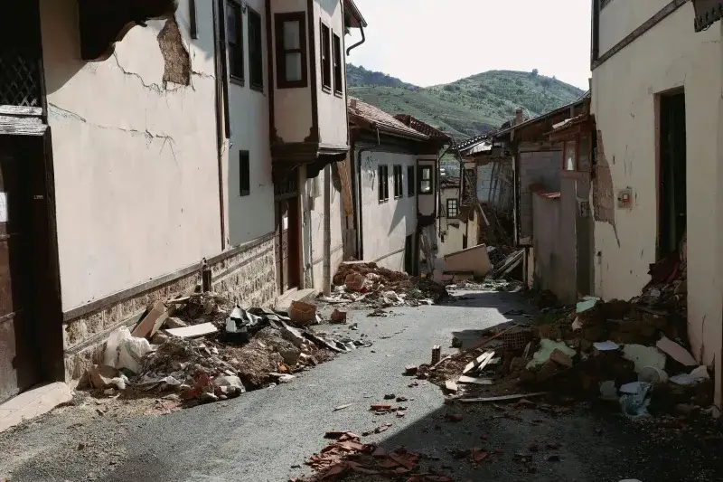Devastation from an earthquake shown on a narrow village street in Malatya, Turkey, with debris and ruined buildings.