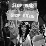 Black and white photo of a woman holding a banner reading 'Stop War, Stop Putin' during a protest.