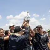 A joyful team celebrates a victory by holding a trophy under a blue sky in Mexico.