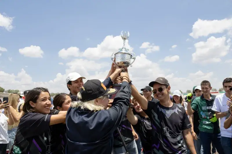 A joyful team celebrates a victory by holding a trophy under a blue sky in Mexico.