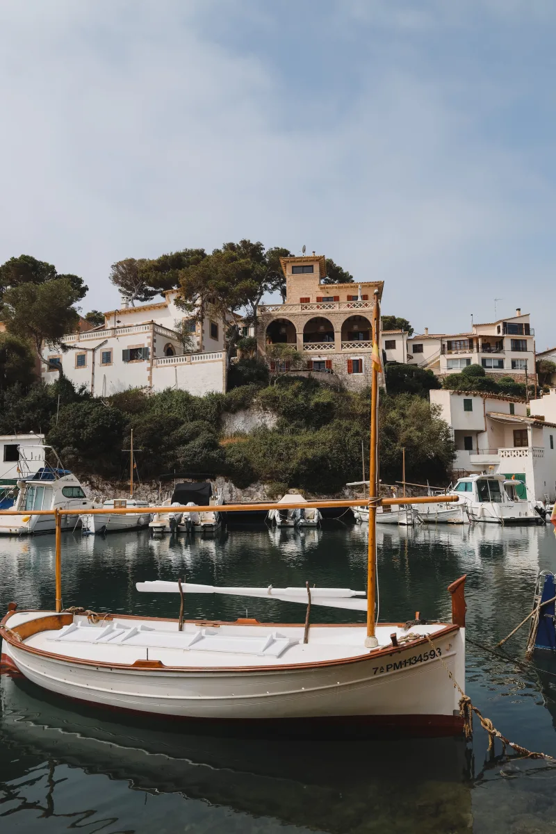 A peaceful view of boats docked at the harbor in Cala Figuera, with charming houses lining the hillside.