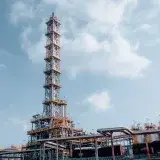 A vertical shot of an oil refinery tower in Trzebinia, showcasing industrial architecture against a blue sky.