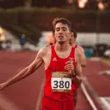 A young male runner crossing the finish line on a track, demonstrating determination and effort.