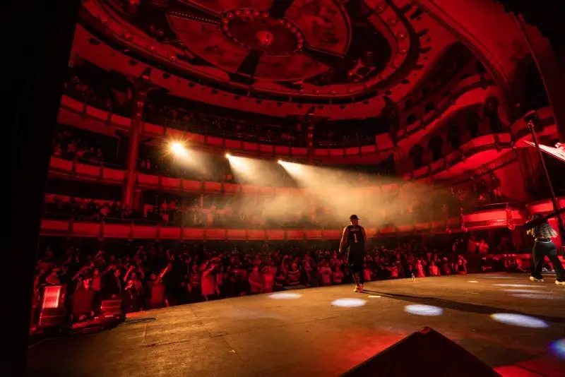 Live performance at Teatro de la Ciudad, Mexico City, with a dynamic audience and performers on a red-lit stage.