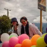 Two women dressed as clowns enjoying a vibrant festival in Mérida, Venezuela with colorful balloons.
