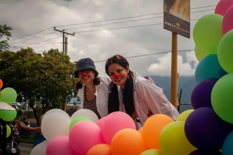 Two women dressed as clowns enjoying a vibrant festival in Mérida, Venezuela with colorful balloons.