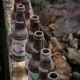 A row of empty beer bottles on a stone wall, set against a rustic outdoor background in Mérida, Venezuela.