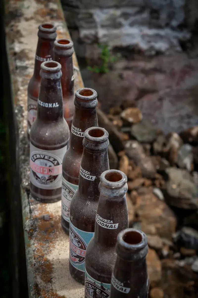 A row of empty beer bottles on a stone wall, set against a rustic outdoor background in Mérida, Venezuela.
