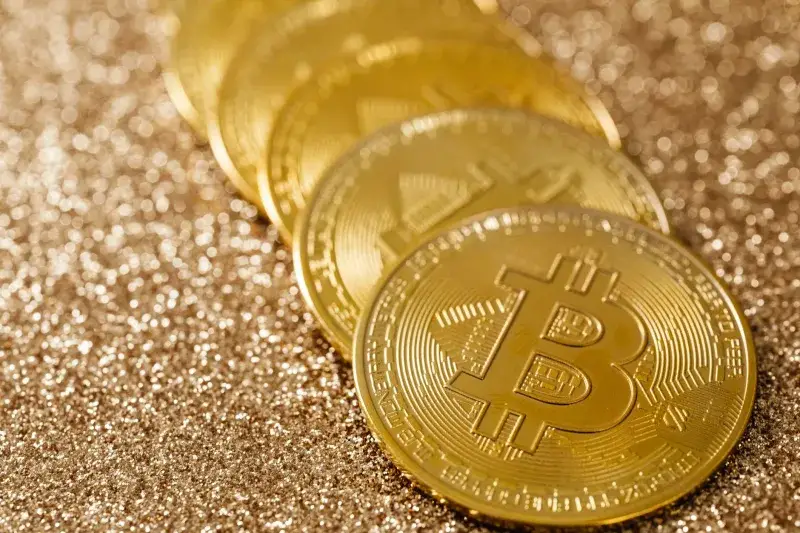 Close-up of golden Bitcoin coins on a shimmering glitter background, symbolizing digital currency's allure.