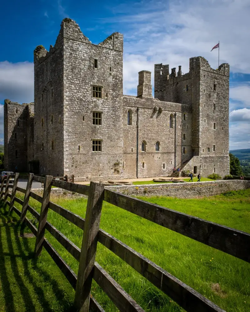 Stunning view of medieval Bolton Castle amidst green grass and a clear blue sky in England.